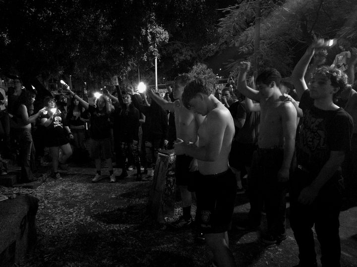 A packed all-ages crowd pressed to the front of an outdoor night gig, fists and phone lights up